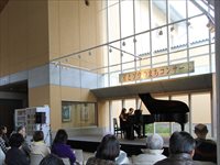 屋内ホールでピアノの演奏が行われ観客が座って鑑賞しているコンサートの写真