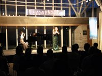 ホールの舞台上で出演者が演奏し客席が静かに聴き入っている様子の写真