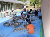 屋外の建物脇で親子が集まって発掘体験をしている様子の写真