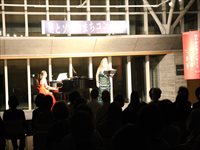 ホールの舞台上で歌う出演者と演奏者を客席が見守っている写真