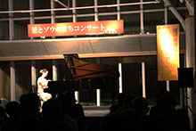 ホールの舞台上でピアノ演奏を行う出演者を客席が鑑賞している写真