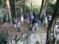 森林の岩場周辺で参加者たちが集まり自然観察をしている写真