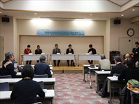 会議室で登壇者が並び参加者が着席してシンポジウムを聴講している写真