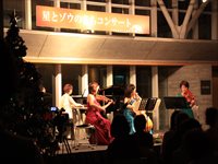 ホールの舞台上で弦楽器を出演者たちが演奏し客席が鑑賞している写真