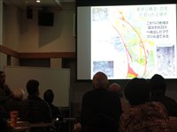 会場のスクリーン前で資料を投影し資料を解説している発表の写真