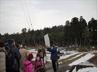 雪の残る山間部で参加者たちが説明を聞きながら散策をしている写真