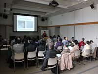 会議室で研究発表を行う登壇者と着席して話を聞く参加者の写真