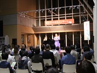 屋内ホールの舞台上で出演者が照明を浴びながら演奏している様子を客席から写した写真