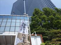 建物の前で旗が掲げられた入口と周囲の緑を正面から写した写真