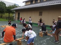 屋外の広場で親子や子供たちが体験活動をしている様子を横から写した写真