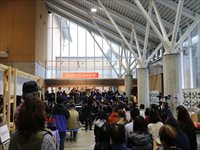 屋内ホールの入口付近で多くの来場者が並びイベントの開始を待っている様子を後ろから写した写真