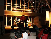 夜の屋内ステージでピアノと弦楽器の演奏者たちが演奏している様子を客席から写した写真