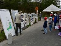 屋外の通路で展示パネルを前に職員が子どもたちに説明をしている写真