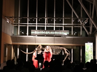 ホールの舞台上で出演者たちが照明を浴びてパフォーマンスをしている写真