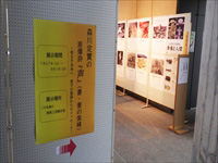 壁に誘導ポスターが貼られ、誘導先ではパーテーションに沢山の展示品が飾られている写真