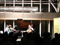 ホールの舞台上で弦楽器を演奏する出演者たちがコンサートを行っている写真