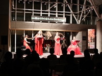 ホールの舞台上で赤い衣装を着た出演者たちが演目を披露している写真