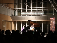 ホールの舞台上で演奏者が照明を浴びてコンサートを行っている様子を撮った写真