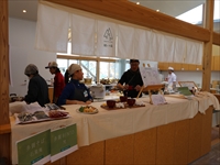 施設内のカウンターで職員たちが食品や資料を並べて来場者を迎えている写真