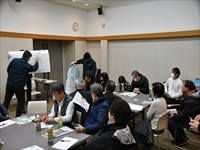 会議室で講師が資料を示しながら参加者たちが着席して説明を聞いている写真