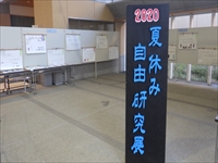 展示場の入口に「夏休み自由研究展」と黒地に青文字で書かれた案内板が置かれている写真
