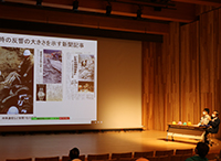 講堂で登壇者がスクリーンを使って講演をしている写真