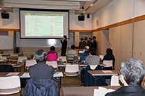 研修室でスクリーンを前に複数の発表者が並び研究発表を行っている写真