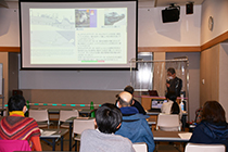 研修室でスクリーンを前に講師が説明を行い参加者たちが着席して聞いている写真
