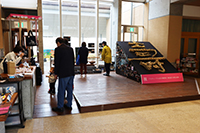 博物館ロビーで受付と展示コーナーが並ぶイベント会場全景の写真