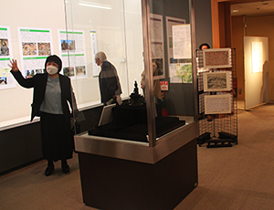 展示室で学芸員が展示ケース前で来場者に展示解説をしている写真