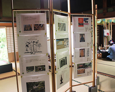 和室で展示パネルの前に座って資料を見ている来場者を写した写真