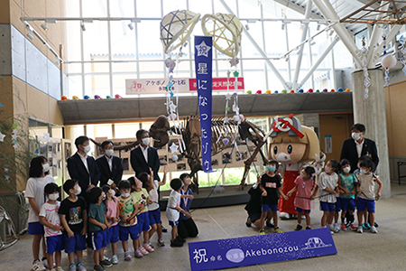 アケボノゾウの標本の前に整列するスーツ姿の男性とその前に整列する児童たちの写真