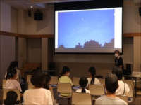 照明の落ちた部屋でスクリーンを見ている子供たちの写真