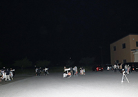 夜の屋外で参加者が望遠鏡を使って星空観察をしている写真