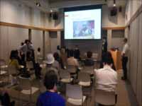 椅子の並べられた部屋で着席しながらスクリーンに映された写真を見ている参加者の後ろ姿の写真