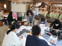 博物館ロビーで参加者がテーブルで工作や作業体験をしている写真