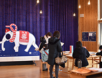 ステージ前で来場者が展示パネルを見ている博物館ロビーの様子の写真