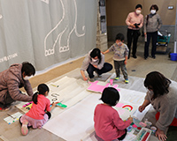 子どもたちが床に紙を広げてお絵描きや工作をしている体験コーナーの写真