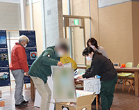 受付テーブルで来場者がアンケート用紙を記入してスタッフが対応している写真