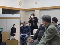 会場で参加者が座ってスタッフの説明を聞いている意見交換会の写真