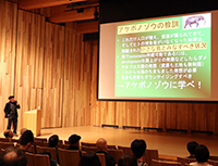 講堂でスクリーンに資料を映し講師が講演している様子の写真