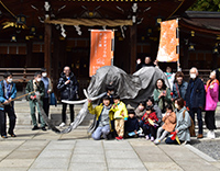 夜の神社境内でナウマンゾウの模型の前に集まった参加者が記念撮影している写真