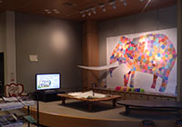 展示室でナウマンゾウの立体展示と壁面アートが並ぶ展示風景の写真