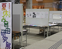 展示会場の入口付近に夏休みの自由研究展の案内パネルが設置されている写真