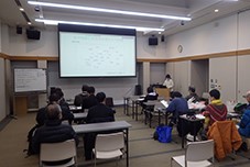 研修室でスクリーンを前に講師が説明を行い参加者たちが着席して聞いている写真