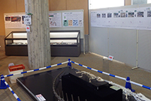 展示会場の中央で展示台と解説パネルが配置されている様子の写真