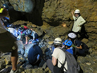 洞窟内でヘルメットを着用した男性が岩肌を触りながら説明している様子の写真