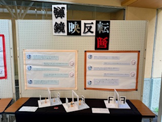 展示スペースで鏡映反転をテーマにした解説パネルと資料が並ぶ展示台の写真