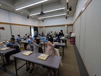 研修室で机に向かって参加者たちが英語の学習をしながら切り餅を切る体験に取り組んでいる写真