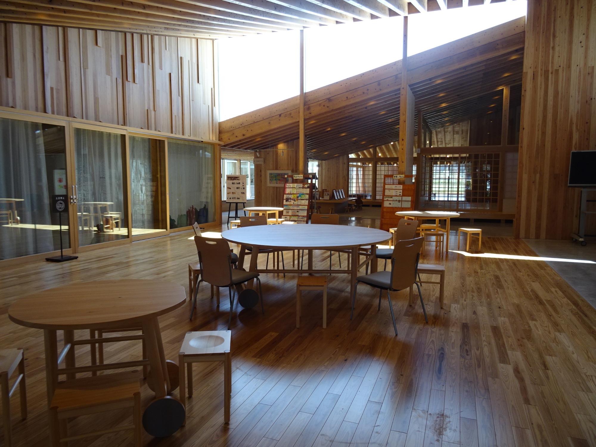 丸テーブルと椅子が配置された木造のエントランスホールを奥まで全体を写した写真